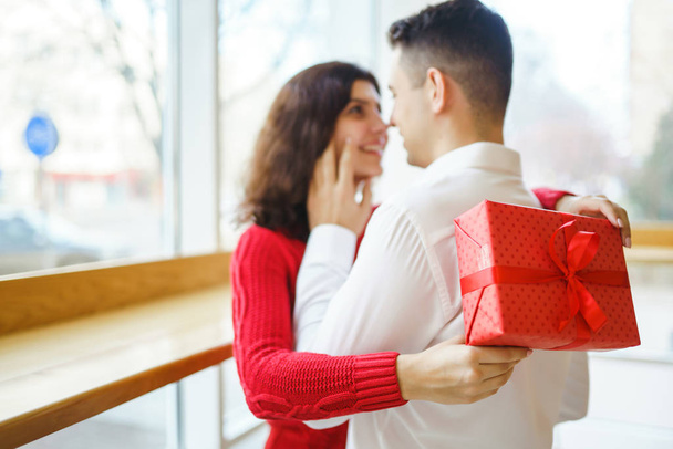Happy couple with gift hugging. Red gift box in the hands of a couple in love. Valentine's Day, holiday and surprise concept. Lovers give each other presents. Relationship and love concept. - Valokuva, kuva