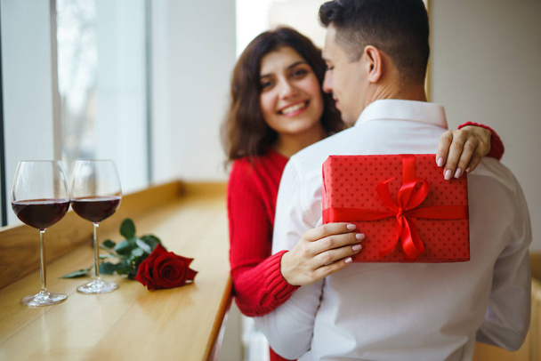 Happy couple with gift hugging. Red gift box in the hands of a couple in love. Valentine's Day, holiday and surprise concept. Lovers give each other presents. Relationship and love concept. - 写真・画像