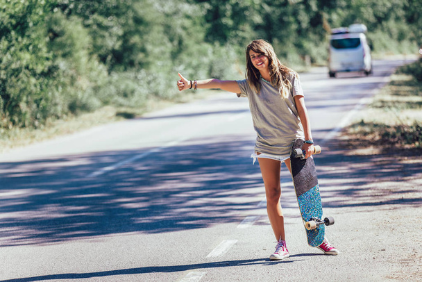 スケートボードの女の子ヒッチハイクと親指で車を停止 - 写真・画像