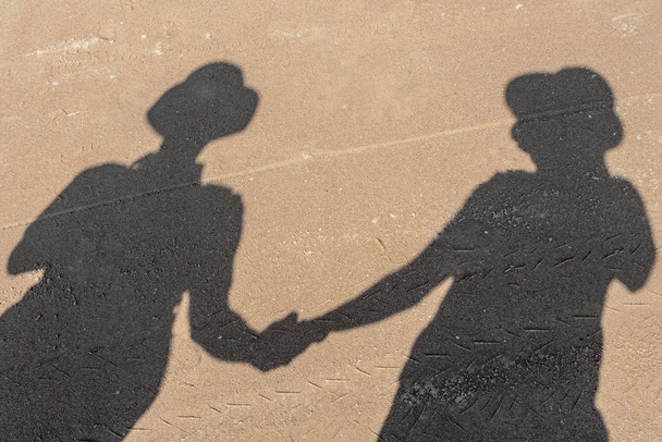 Foto de sombras grises en la arena amarilla de una joven pareja enamorada hombre y mujer en la playa en verano. Mano a mano
 - Foto, Imagen
