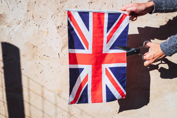 A woman cuts with scissors the British flag in protest. - Photo, Image