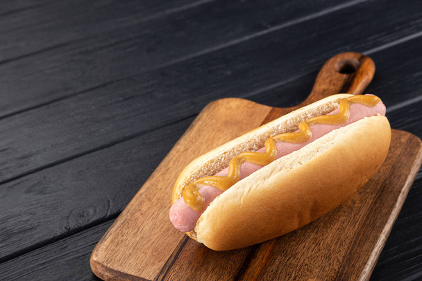Hot dogi z musztardą na drewnianej desce. Hot dogi serwowane na czarnym stole. Wolne miejsce na tekst - Zdjęcie, obraz