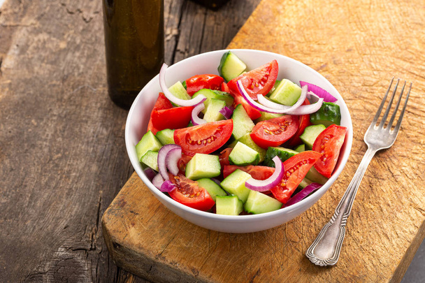 Salad of tomatoes and cucumbers in a plate and vegetables on a wooden table - Photo, Image