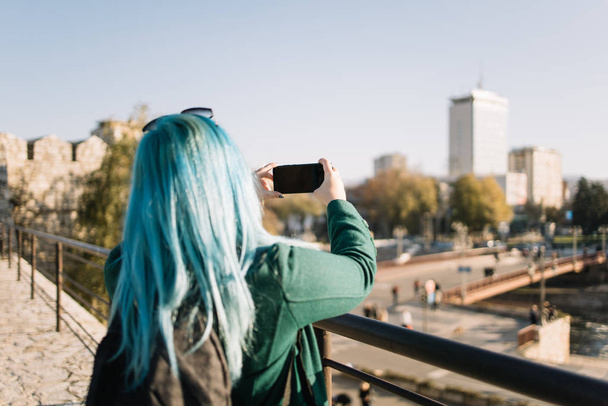 Дівчина з блакитним волоссям дивиться її відображення на смартфон
 - Фото, зображення