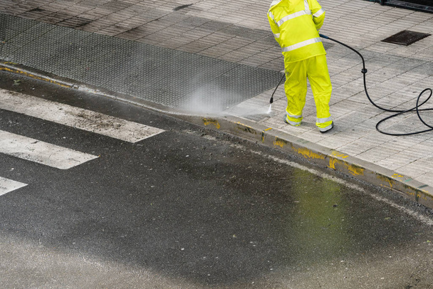 Рабочий очищает тротуар водой под давлением. Концепция технического обслуживания или очистки - Фото, изображение