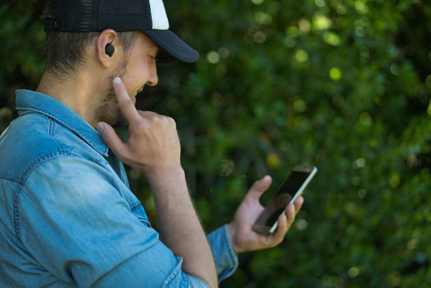 Młody człowiek słuchający muzyki z bezprzewodowymi słuchawkami i smartfonem. Koncepcja techniczna - Zdjęcie, obraz