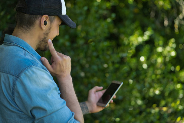 Mladý muž poslouchá hudbu s bezdrátovými sluchátky a smartphonem.  - Fotografie, Obrázek