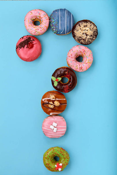 Знак вопроса из глазированных красочных пончиков на синем фоне
 - Фото, изображение
