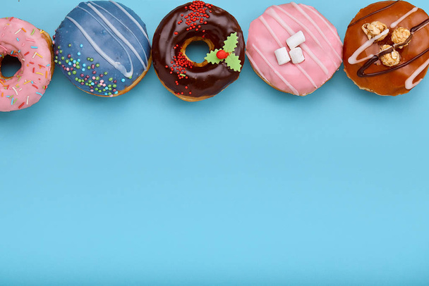 Top view of assorted donuts on blue background with copy space. Colorful donuts background. Various glazed doughnuts with sprinkles. - Photo, Image