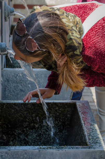 Kastanienfrau trinkt Wasser aus dem Auslauf eines Brunnens - Foto, Bild