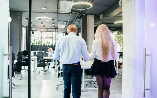 Stylish young man and woman at official style clothes which walking through the office room. - Foto, Imagen