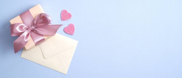 Valentine gift box with pink ribbon bow and envelope with love letter on paste blue background. Banner design for St Valentines Day, Mothers Day, anniversary. Love and romance concept. - 写真・画像