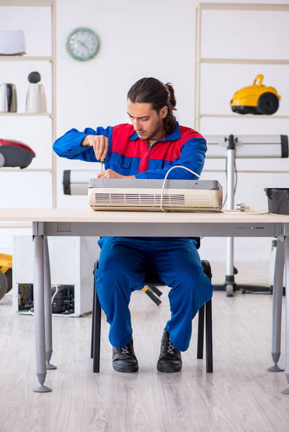Молодой мужчина-подрядчик ремонтирует кондиционер в мастерской
 - Фото, изображение