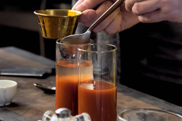 Χύνοντας χυμό ντομάτας σε ποτήρια μέσω κουταλιού. - Φωτογραφία, εικόνα
