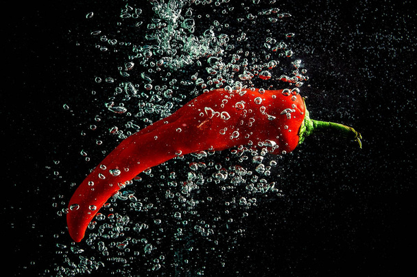 Fresh red chilli peppers are thrown into the water with bubbles - Zdjęcie, obraz
