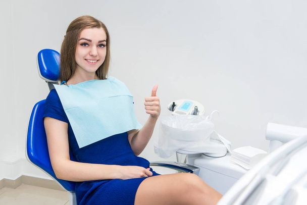 Young girl patient smiles and shows thumb up in the doctor's chair in the dental office - Фото, изображение
