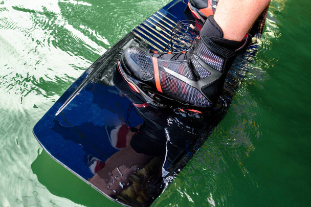 Ausrüstung für Wakeboarding. Männerfüße auf dem Wakeboard im Wasser und Vorbereitung auf das Wakeboarding - Foto, Bild