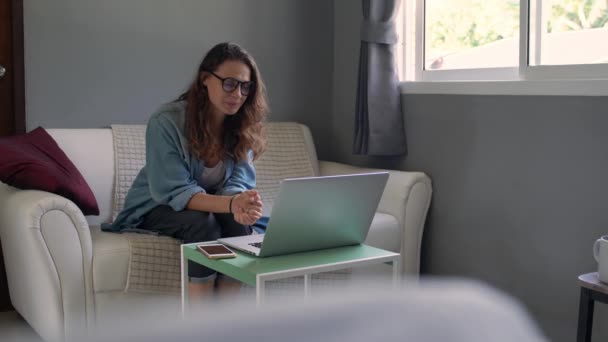 A young woman with a laptop sitting on a sofa and holds an online consultation. - Metraje, vídeo