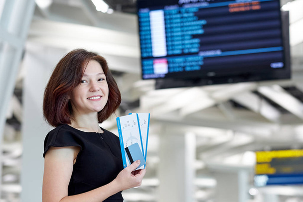 Business woman with tickets and credit card waiting for departure near the information board in airport - Foto, Imagen