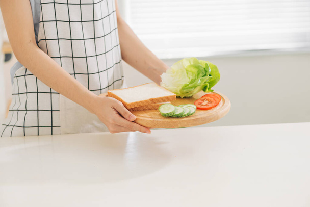 making sandwich with bread, cheese, salad and ham with hands on wooden cutting board - Photo, Image
