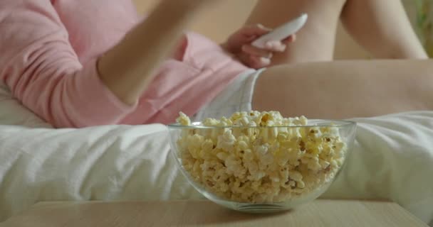 Mujer viendo la televisión en el dormitorio acostada en la cama y comiendo palomitas de maíz
 - Metraje, vídeo