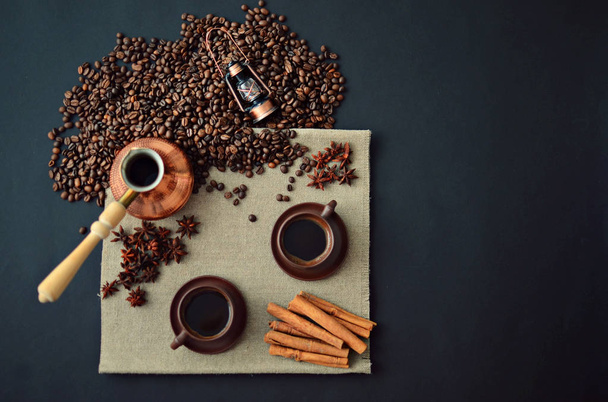 Cooper Turkish coffee pot, two cups of coffee, coffee beans, cinnamon sticks, star anise, canvas napkin on dark background, top view, copy space - Zdjęcie, obraz