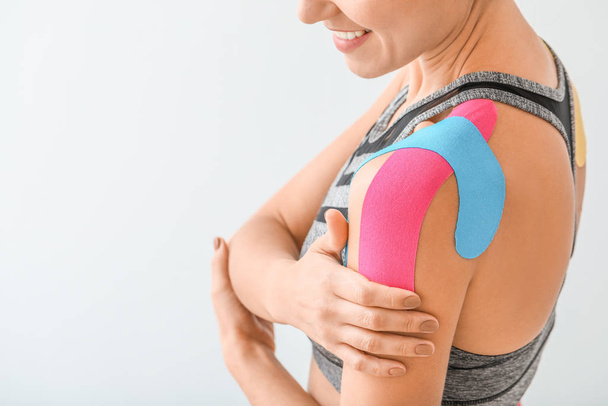 Sporty woman with physio tape applied on shoulder against light background, closeup - Photo, Image