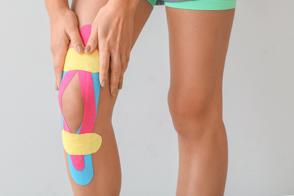 Sportowa kobieta z taśmą fizjologiczną nałożoną na kolano na lekkie tło, zbliżenie - Zdjęcie, obraz