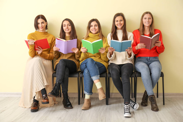 Young women with books sitting near color wall - Zdjęcie, obraz