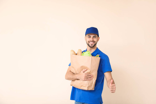 Handsome worker of food delivery service showing thumb-up on color background - Photo, Image