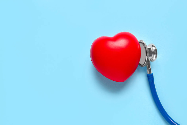 Moderne stethoscoop en rood hart op kleur achtergrond - Foto, afbeelding