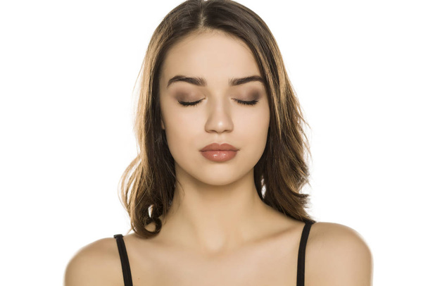 Jonge vrouw met make-up en gesloten ogen, poseren op witte achtergrond - Foto, afbeelding