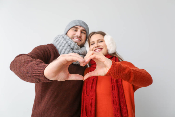 Happy couple in winter clothes making heart shape with their hands on light background - Foto, Bild