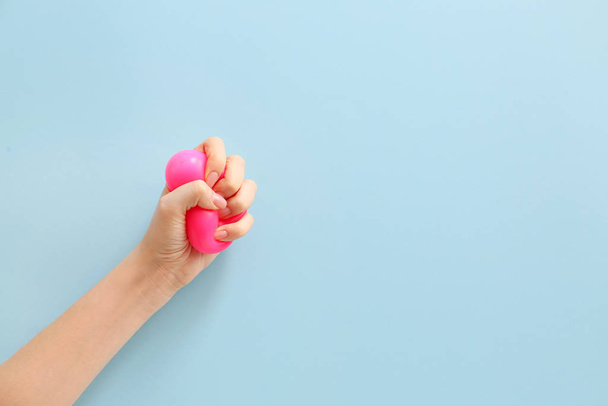 Female hand squeezing stress ball on color background - Photo, image