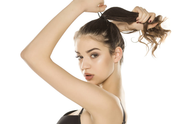 Young woman with makeup  tying her hair on white background - Fotoğraf, Görsel