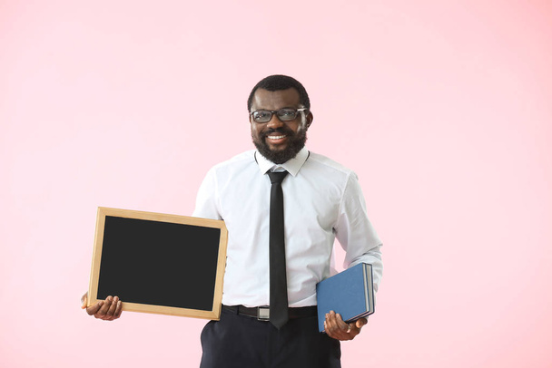 Афроамериканский учитель с доской и книгами на цветном фоне
 - Фото, изображение