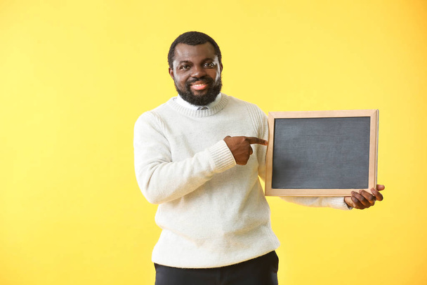 African-American teacher with chalkboard on color background - Fotó, kép
