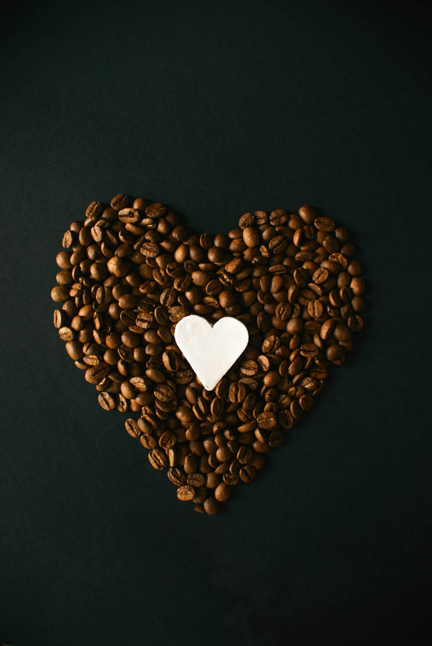 Heart made from coffee beans on a black background with a white clay heart. - Zdjęcie, obraz