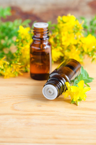 Two small bottles with essential St John's-wort oil (extract, tincture, infusion) on the old wooden background. Aromatherapy, spa and herbal medicine ingredients.  - Фото, зображення
