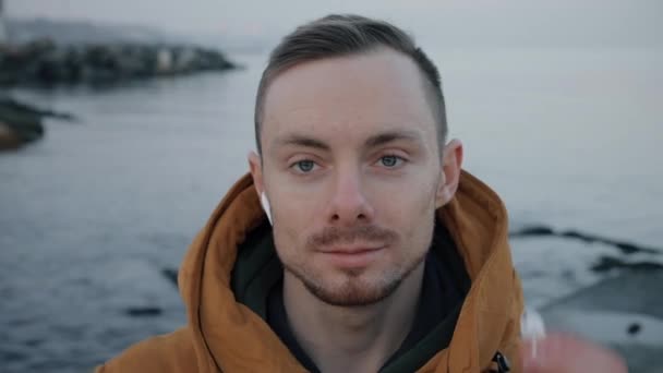 Handsome confident man puts on earphones at the sea beach - Séquence, vidéo