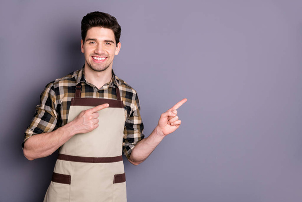 Photo of cheerful positive handsome man smile toothy pointing into empty space working as barista adverting his cafe isolated grey color background - Photo, Image