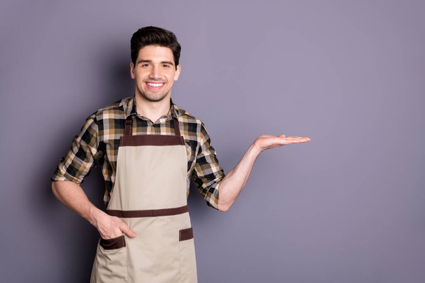 Photo of cheerful positive handsome man with hand in pocket smiling toothy holding empty space in hand with advertising isolated grey color background - Φωτογραφία, εικόνα