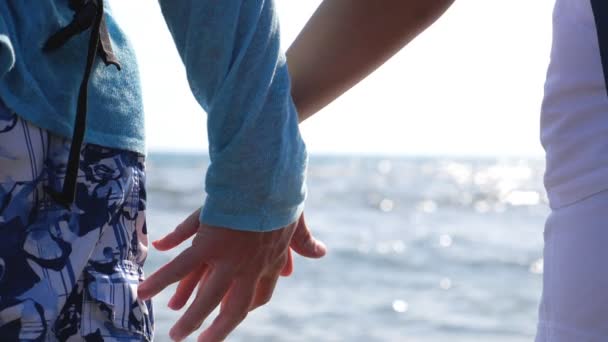 Young pair of lovers holding hands and flirting to each other standing on ocean coast. Couple of travelers spending time together during vacation on resort. Beautiful sunny seascape at background - Footage, Video