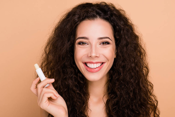 Close-up portrait of nice cute charming lovely attractive winsome feminine cheerful wavy-haired girl applying new useful stick clean clear perfect lips isolated on beige background - Fotó, kép