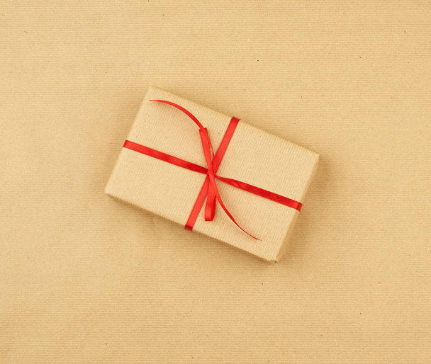 Подарок, завернутый в коричневую крафтовую бумагу и завязанный тонким шелковым ребром
 - Фото, изображение