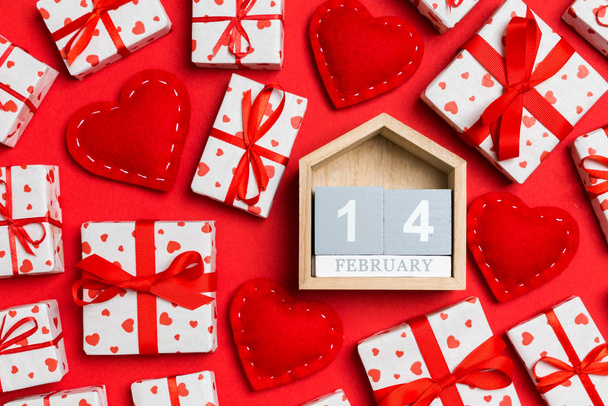 Top view of wooden calendar, white gift boxes and red textile hearts on colorful background. Valentine's Day concept - Photo, Image