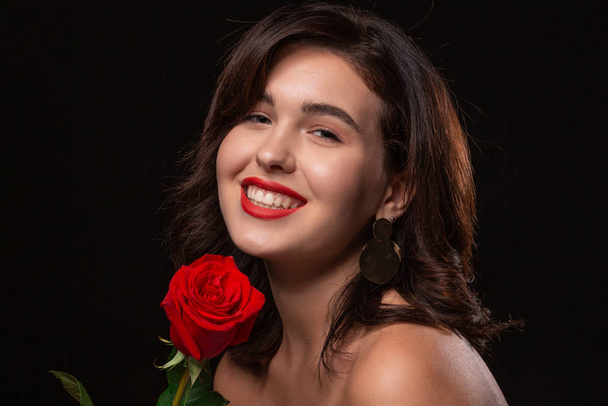 Beautiful woman with bright makeup posing isolated over black background with red rose. - Fotó, kép