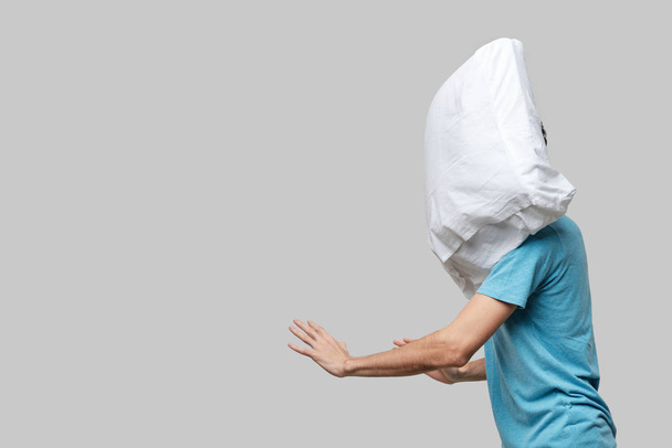 Flying white pillow hitting pretty brunet man in a blue tee. - Photo, image
