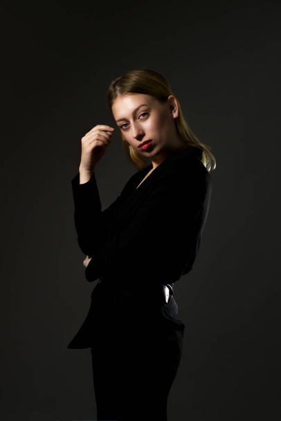 blonde in a black suit on a black background. Business woman - 写真・画像