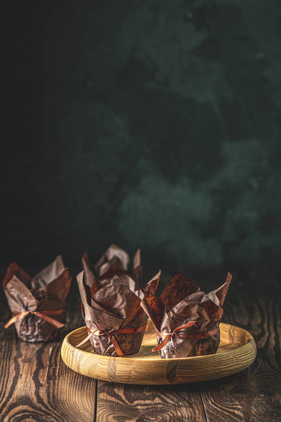 Chocolate muffins in brown paper with ribbon on wooden bowl. Close up, shallow depth of the field, greeting food composition. - Foto, Imagem
